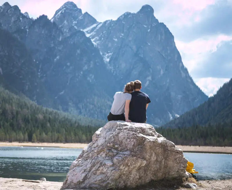 A couple sitting on a large rock by a mountain lake, reflecting peaceful togetherness in nature.
